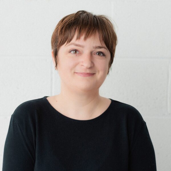 Photo by Bri Hammond. Meg, a short-haired brunette wearing a black shirt, smiles at the camera.