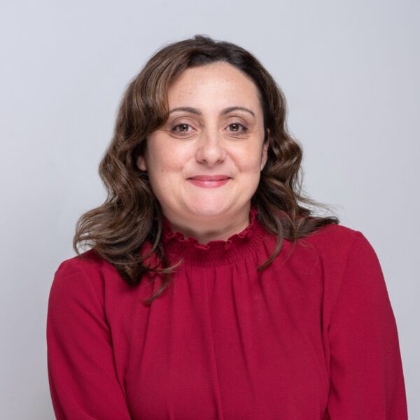 Nadia, a brunette with shoulder-length hair wearing a red blouse, smiles at the camera.